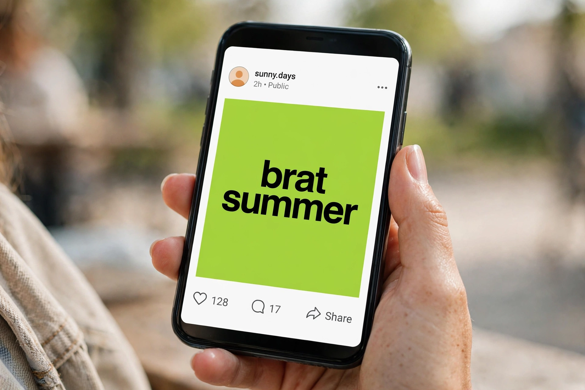 Hand holding a phone showing a social media post with a lime-green tile reading 'brat summer'