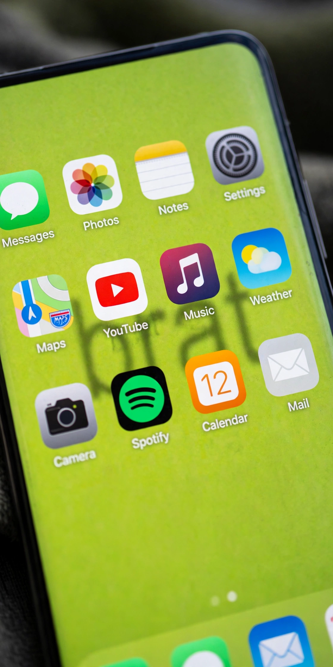 iPhone home screen showing a lime green brat wallpaper generator design with blurry text behind app icons