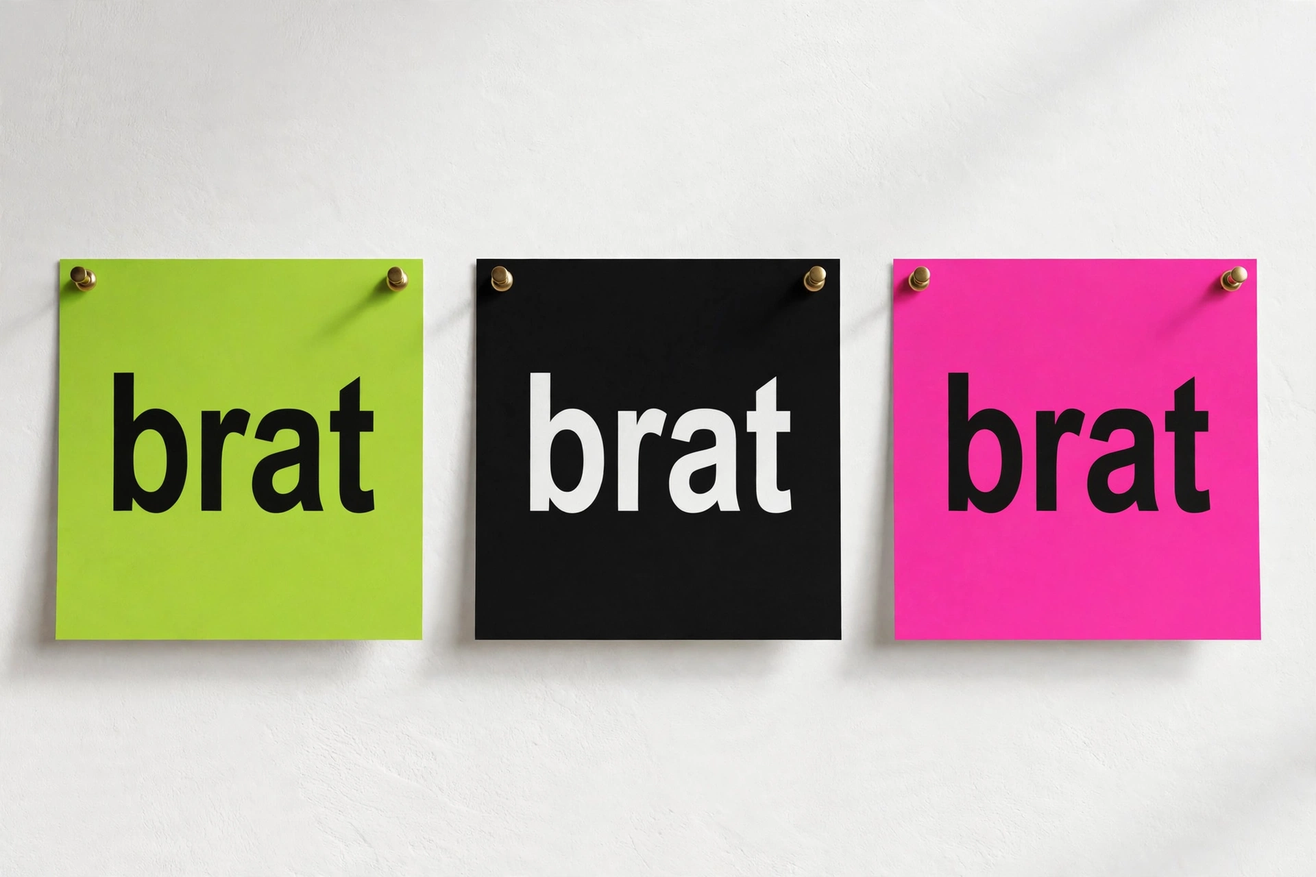 Three brat-style text tiles pinned on a wall: lime green, black, and pink, each reading 'brat' — made with a brat text generator
