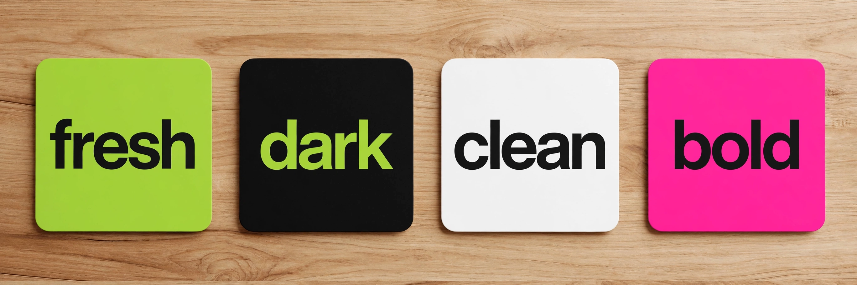 Four square logo tiles on a wooden table: lime green reading 'fresh', black reading 'dark', white reading 'clean', and pink reading 'bold'