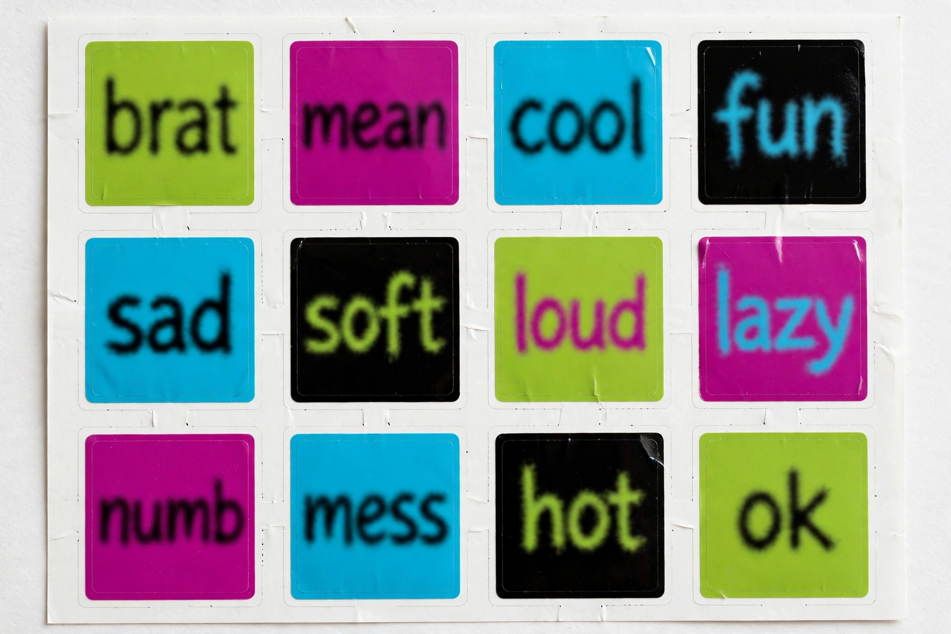 Sticker sheet of twelve square brat-style stickers in green, magenta, cyan and black with words like brat, mean, cool and fun